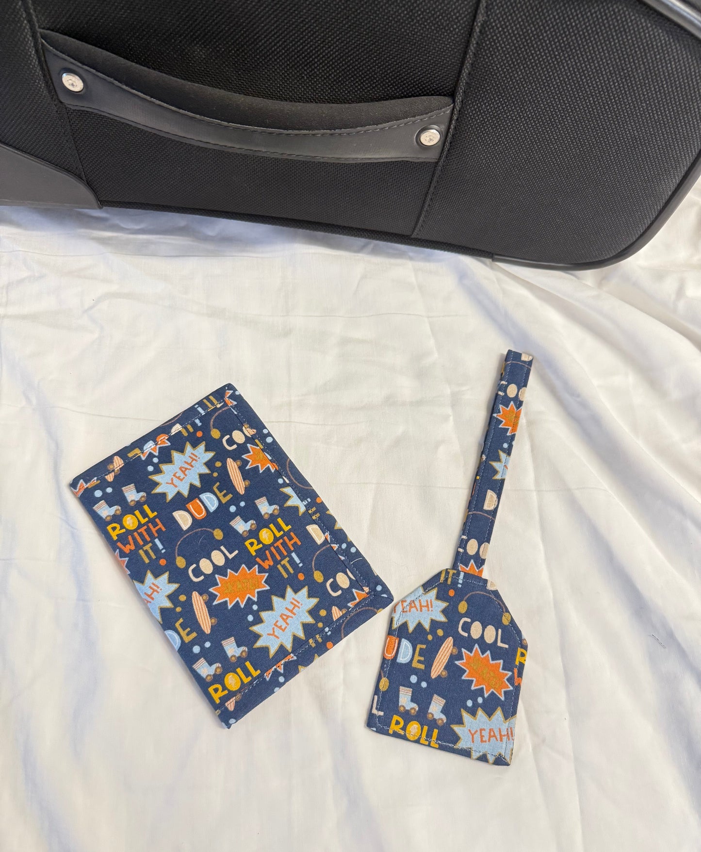 Two blue patterned luggage tags on a white quilt next to a suitcase.