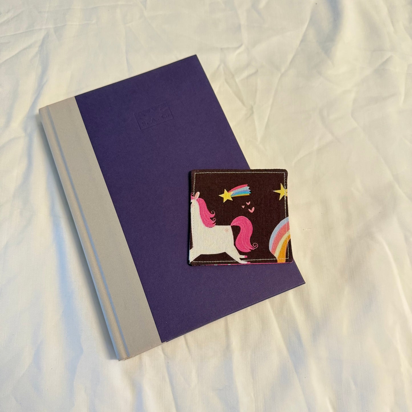 Small notebook with a colorful bookmark featuring a mermaid design on a white fabric background