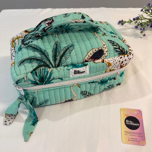A quilted lunch bag with a tropical flamingo and palm print in mint green, displayed on a white fabric surface next to a small branded card.