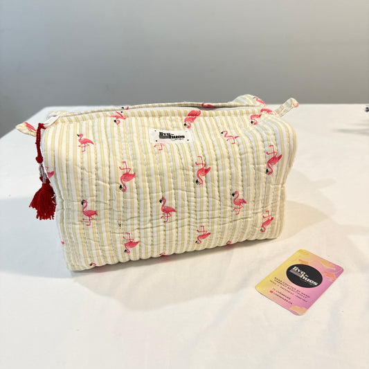 A quilted cosmetic pouch by BoTooism featuring a cream and white vertical stripe pattern with pink flamingos, red tassels, and a small white brand label. A pink and yellow BoTooism gift card is placed next to it on a white surface against a gray background.