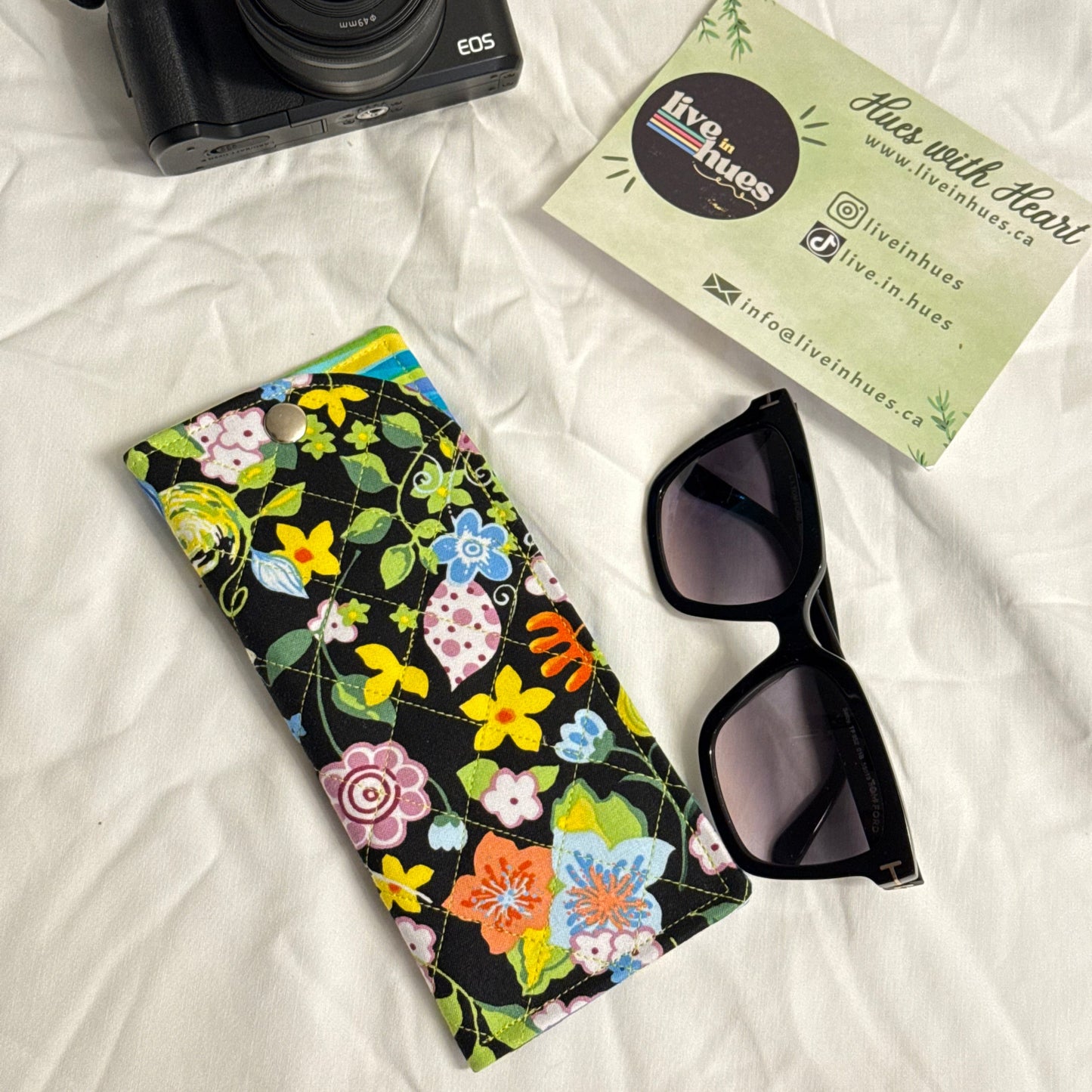 Camera, sunglasses, and floral case on a white surface