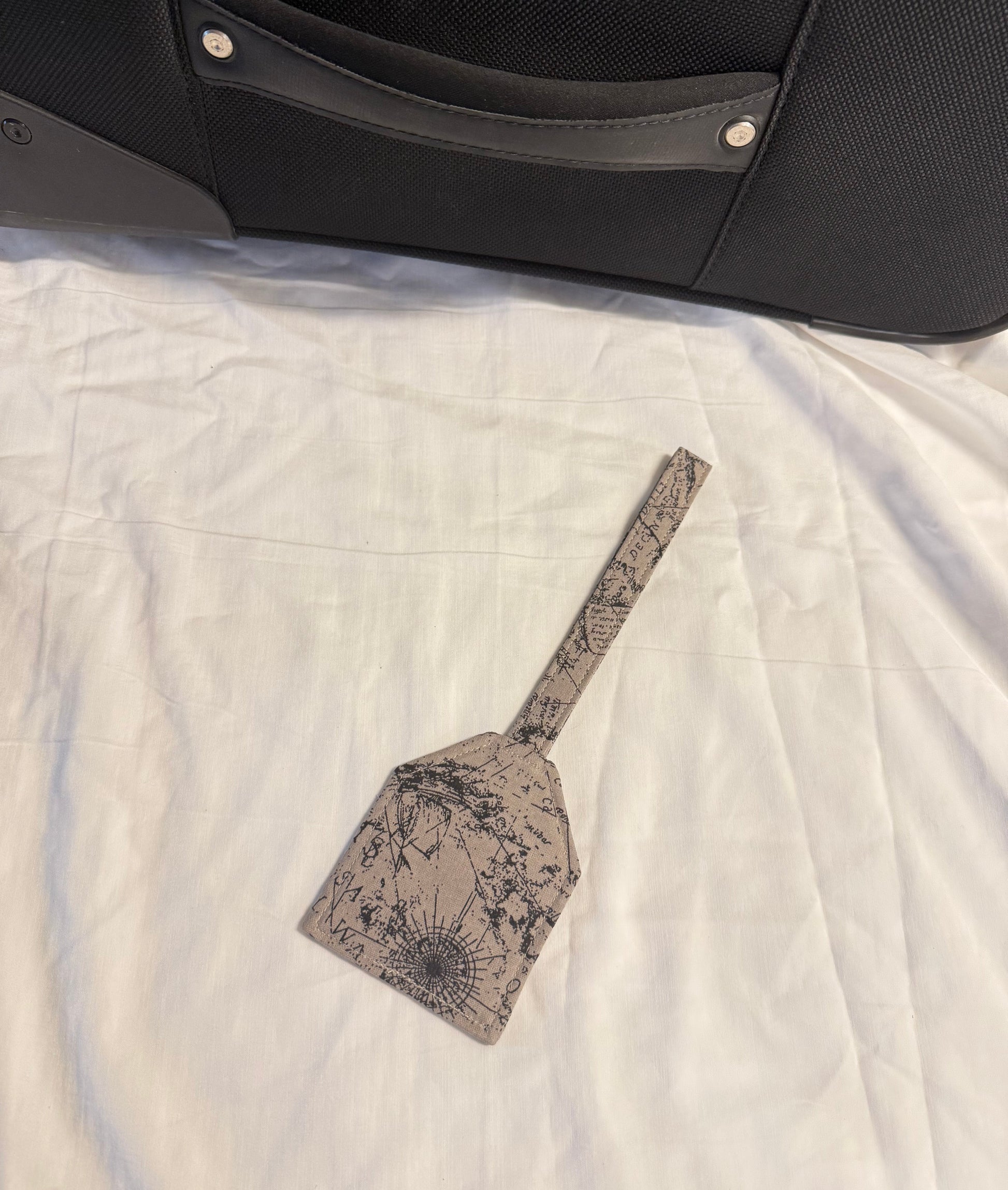 Decorative spatula with floral pattern on a white quilt next to a black bag.
