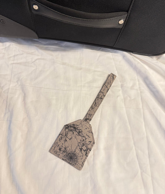 Decorative spatula with floral pattern on a white quilt next to a black bag.