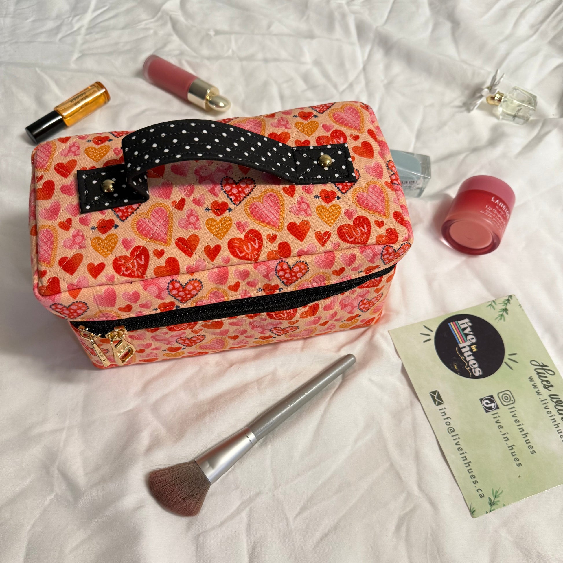 Pink heart-patterned cosmetic bag with makeup items on a white surface