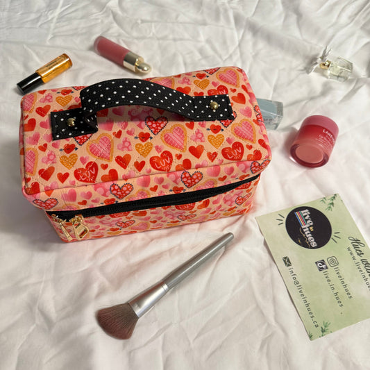 Pink heart-patterned cosmetic bag with makeup items on a white surface