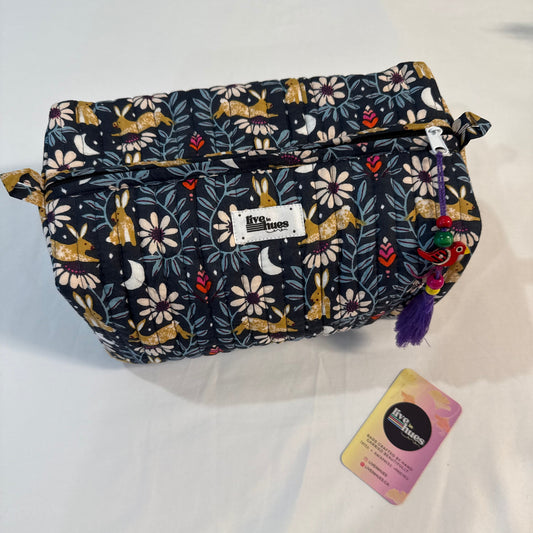 A Kith London cosmetic pouch with a dark navy blue background and a whimsical print of foxes, flowers, and leaves, shown on a white fabric background with its original tag nearby.