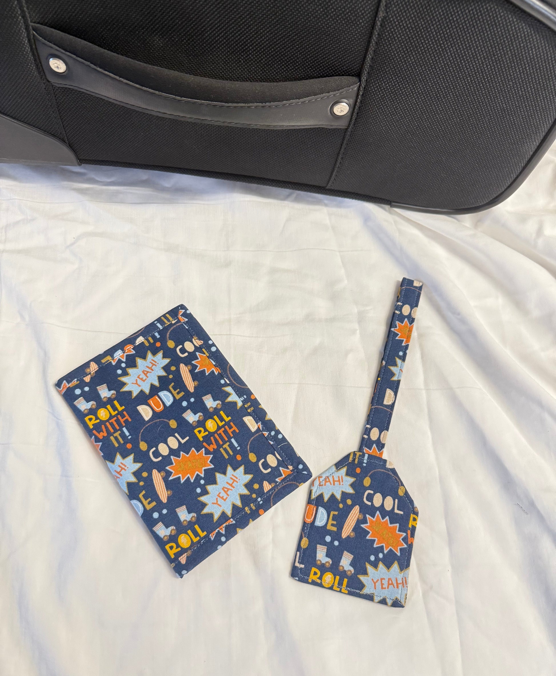 Two blue patterned luggage tags on a white quilt next to a suitcase.
