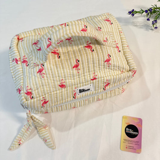 A quilted zippered pouch with a yellow and white striped pattern and pink flamingo print, shown on a white fabric background next to a small card.