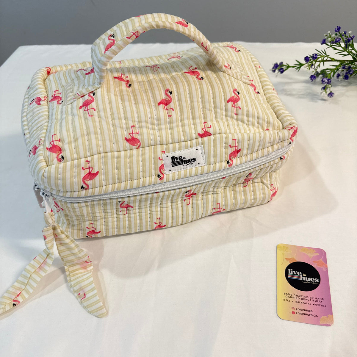 A quilted zippered travel or toiletry case with a top handle, featuring a cream and yellow stripe pattern with pink flamingos. The brand label reads 'Briarwood'.