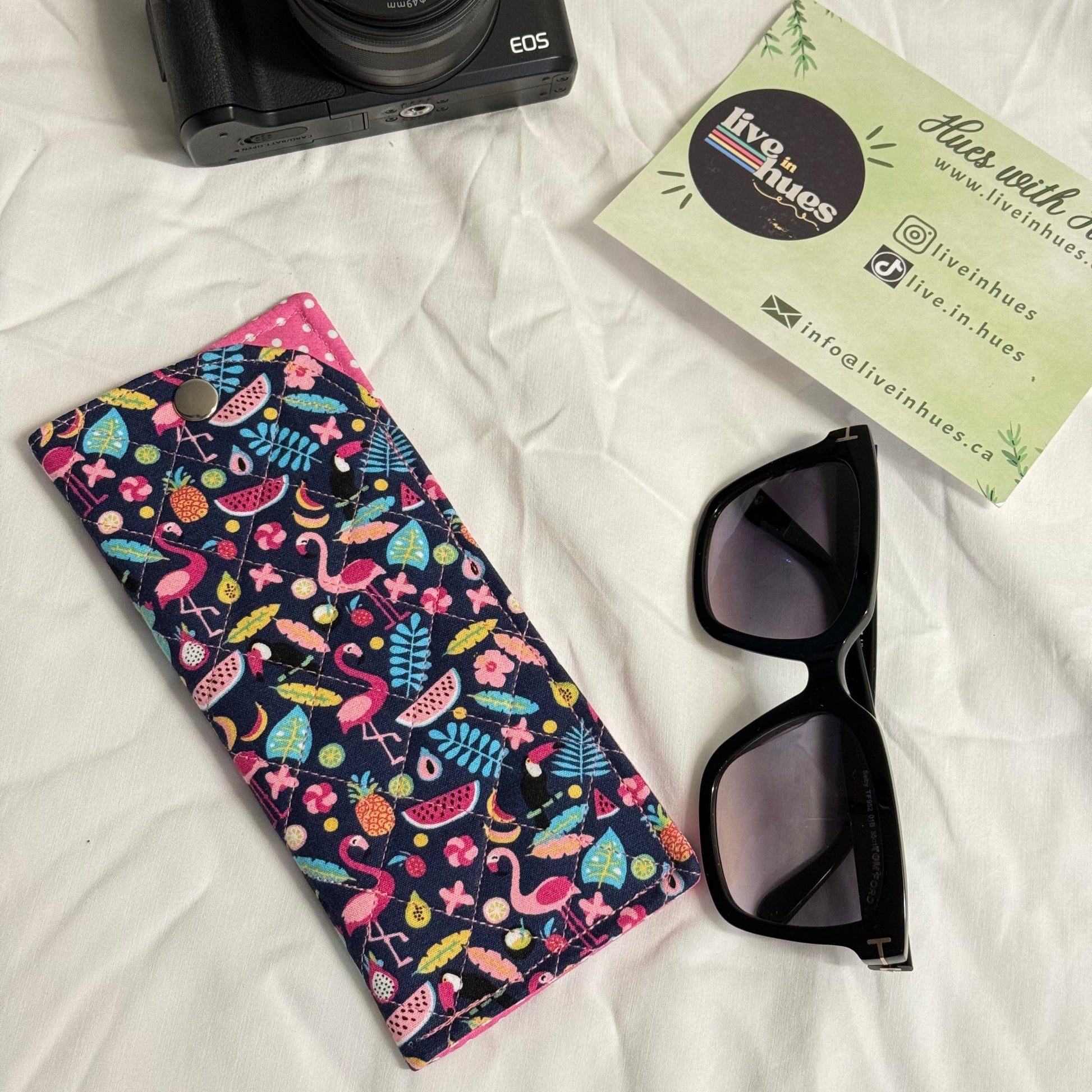 Camera, sunglasses, and patterned case on a white surface with visible brand name.