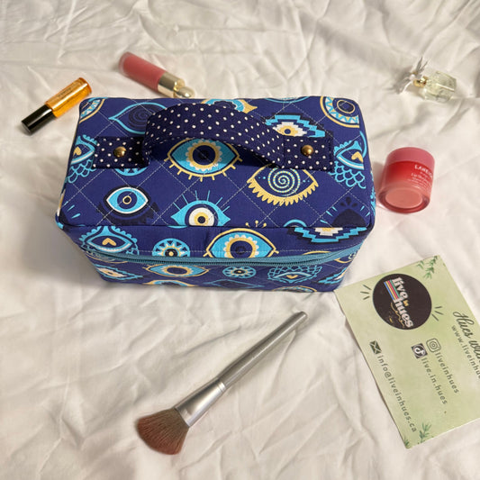 Blue patterned makeup bag with cosmetic items on a white fabric background