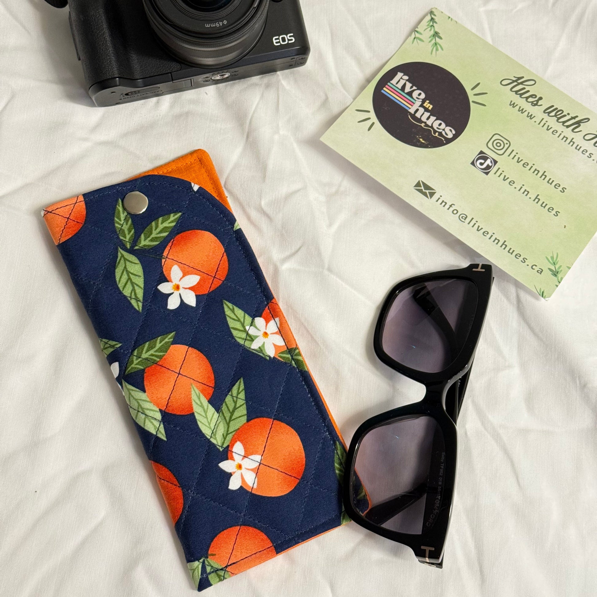 Camera, sunglasses, and a floral-patterned pouch on a white surface