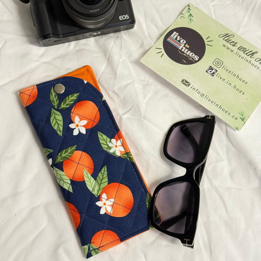 Camera, sunglasses, and a floral-patterned pouch on a white surface