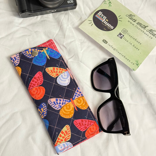 Camera, sunglasses, and colorful heart-patterned case on a white fabric background