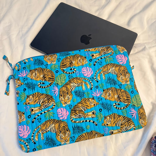 Blue pouch with tiger pattern next to a black laptop on a white fabric background