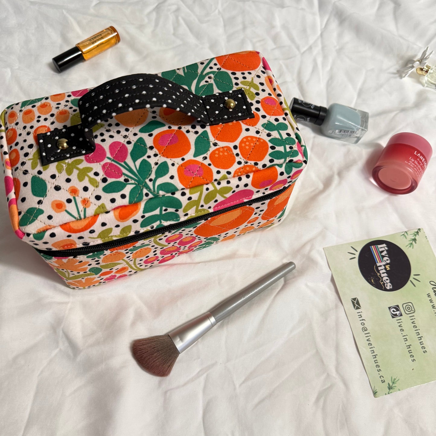 Floral patterned toiletry bag with makeup items on a white surface