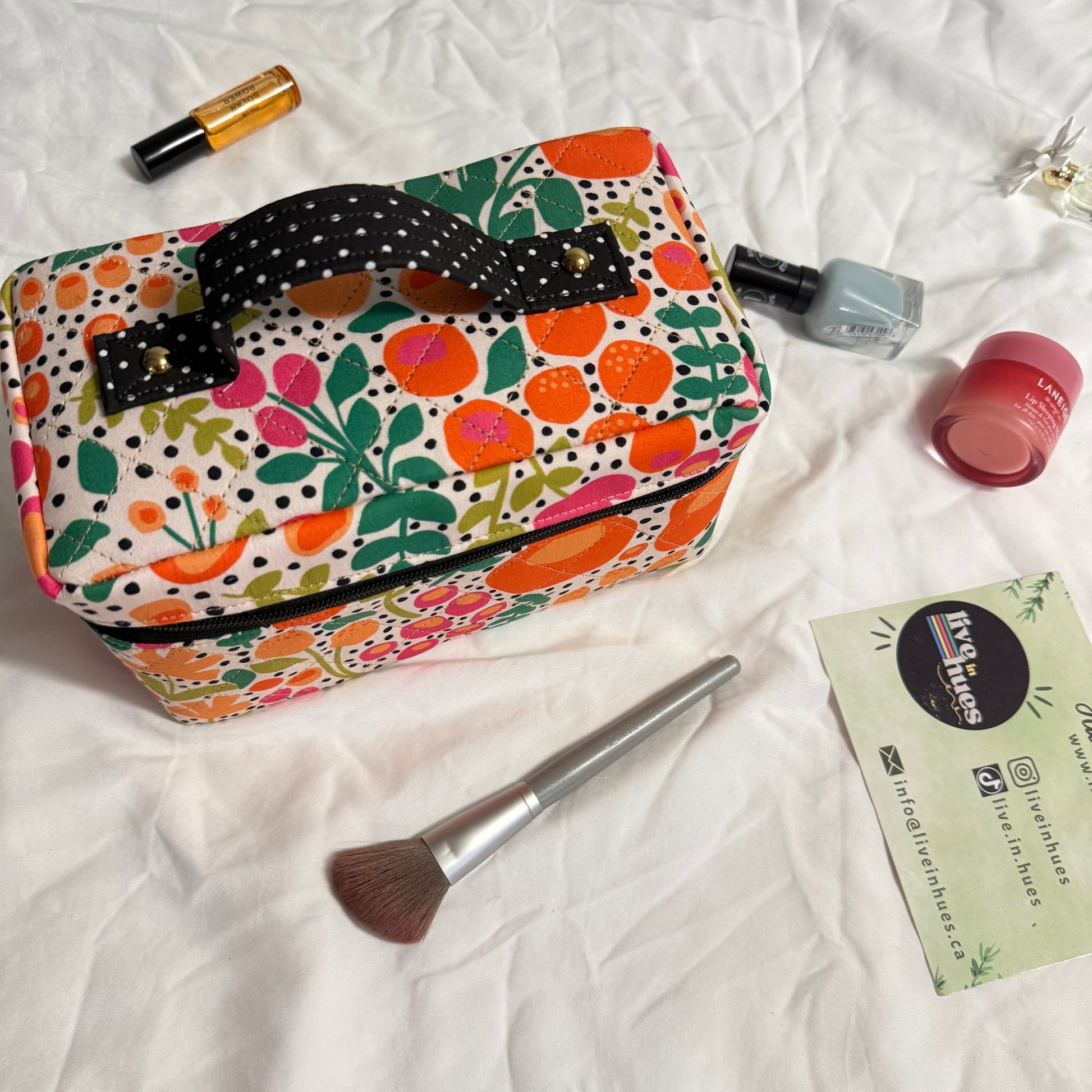 Floral patterned toiletry bag with makeup items on a white surface