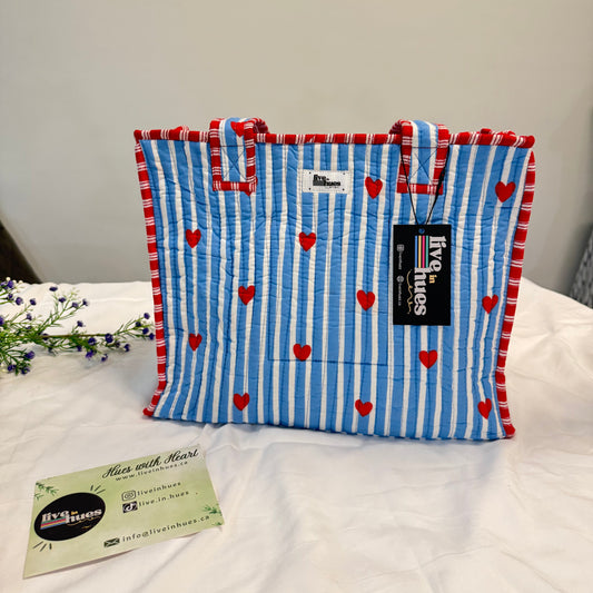 Folded blue and red striped towel with heart patterns on a white surface, featuring a brand label.
