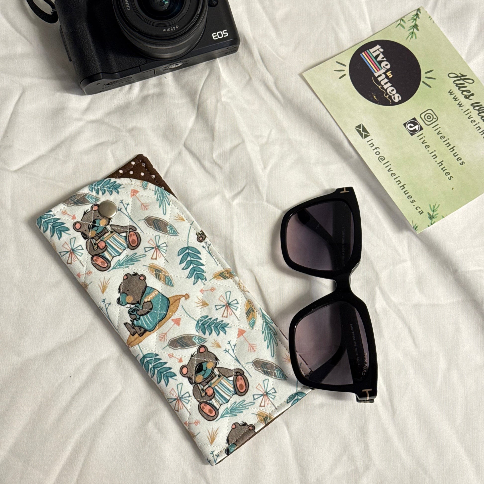 Camera, sunglasses, and patterned case on a white surface with 'live in hues' card.