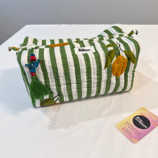 A green and white striped quilted pouch with embroidered lemon details, a tassel charm, and a small white brand label, displayed on a white surface next to a card.