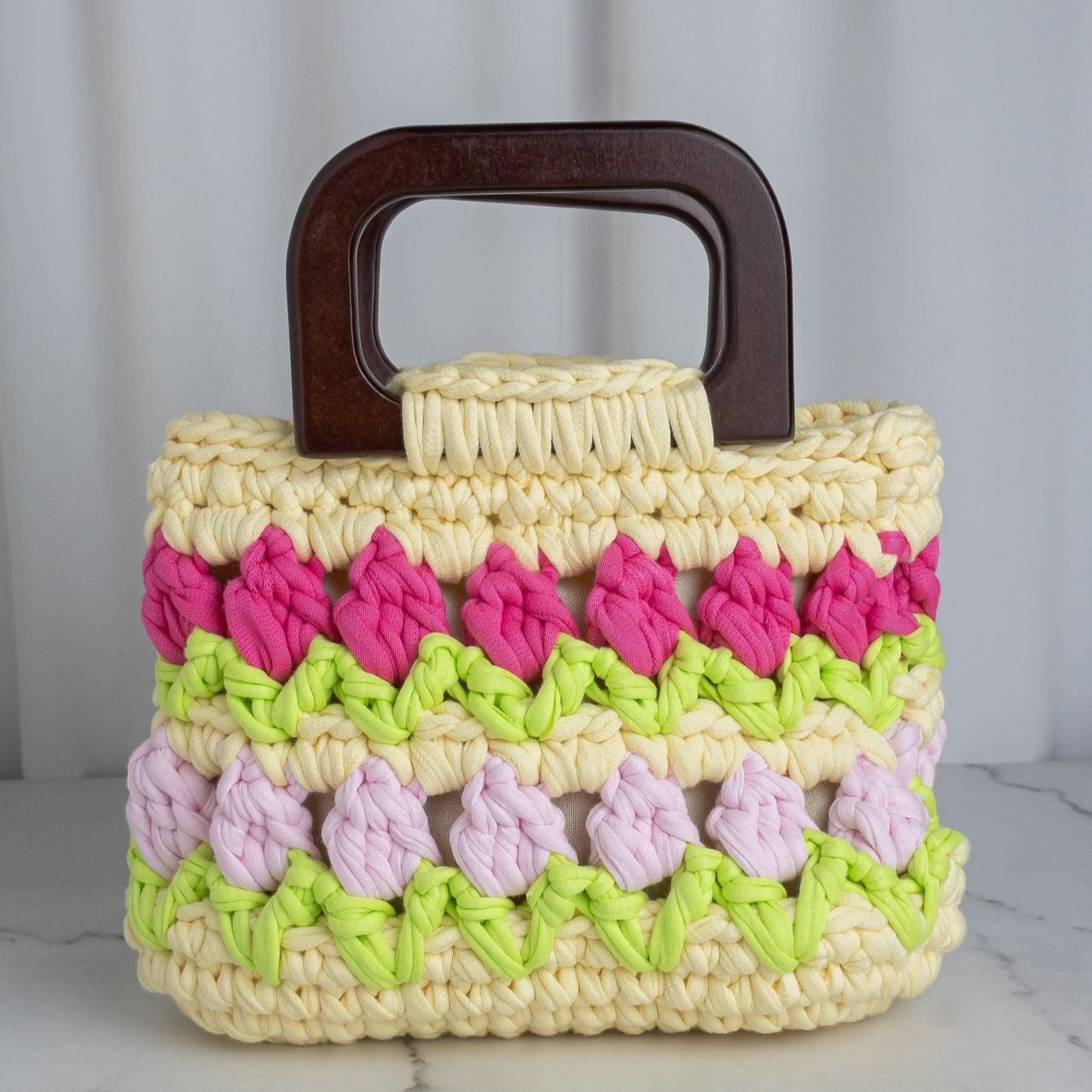 Crocheted handbag with a wooden handle on a marble surface