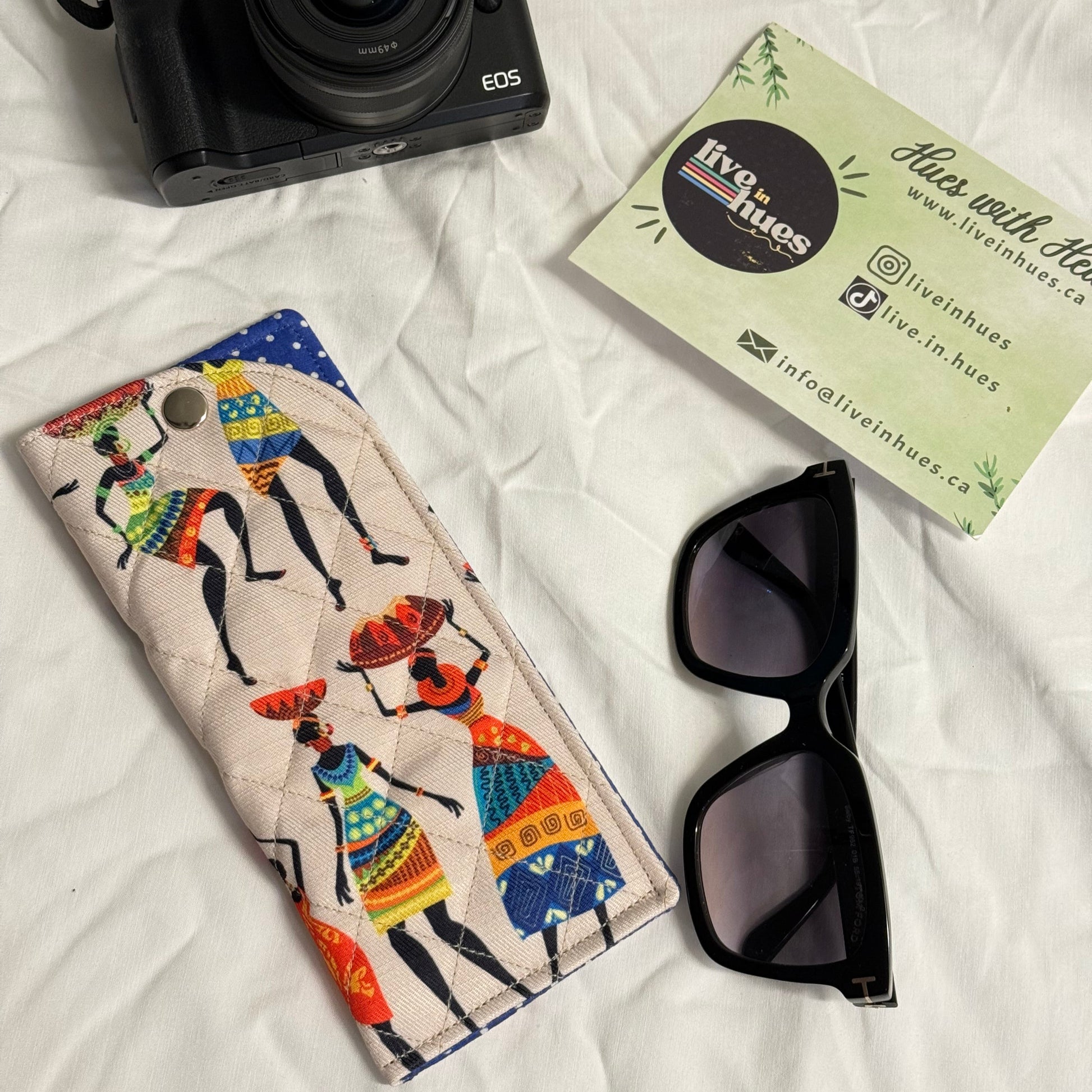 Camera, sunglasses, and a colorful case on a white surface with a business card.