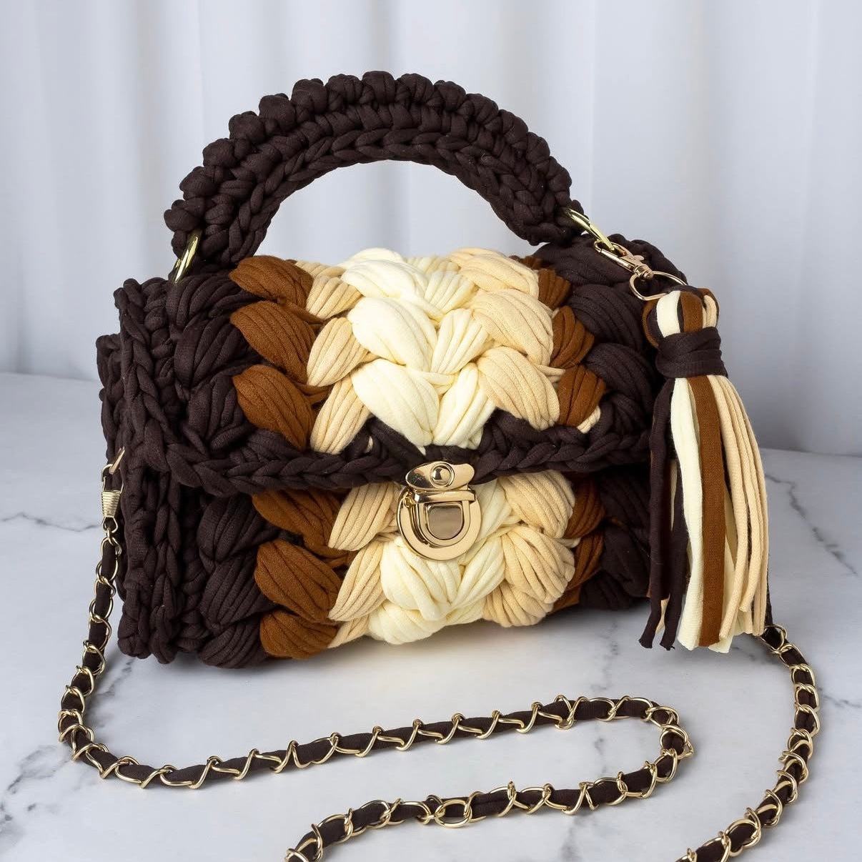 Woven handbag with braided design and tassel on a marble surface