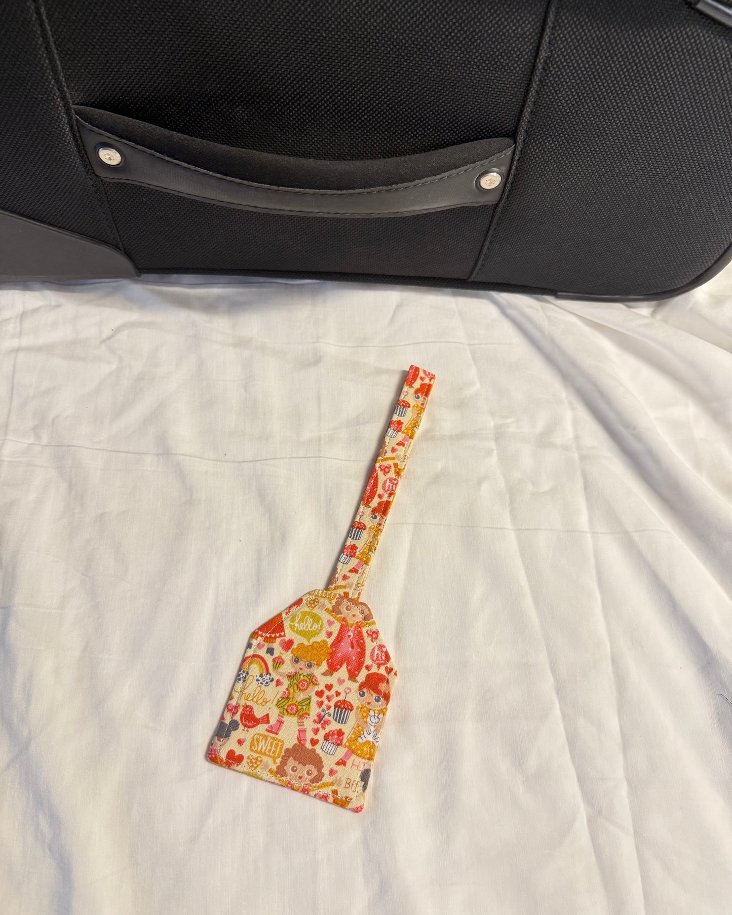 Colorful spatula with cartoon design on a white quilt next to a black suitcase.