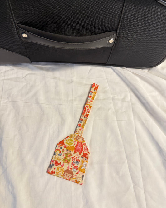 Colorful spatula with cartoon design on a white quilt next to a black suitcase.