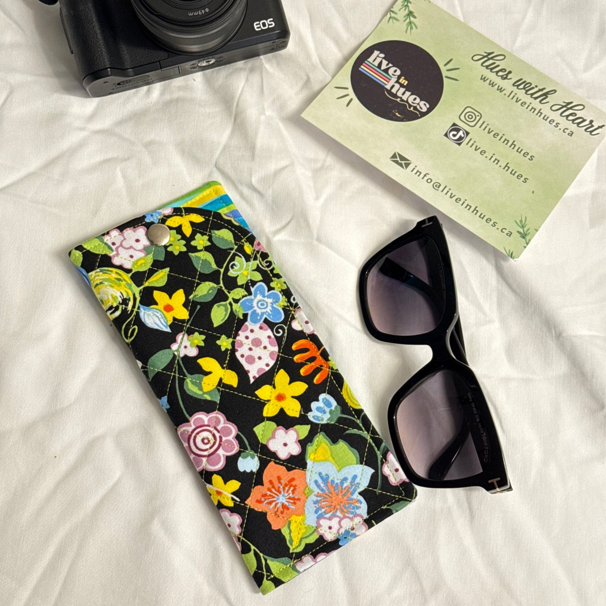 Camera, sunglasses, and floral case on a white surface