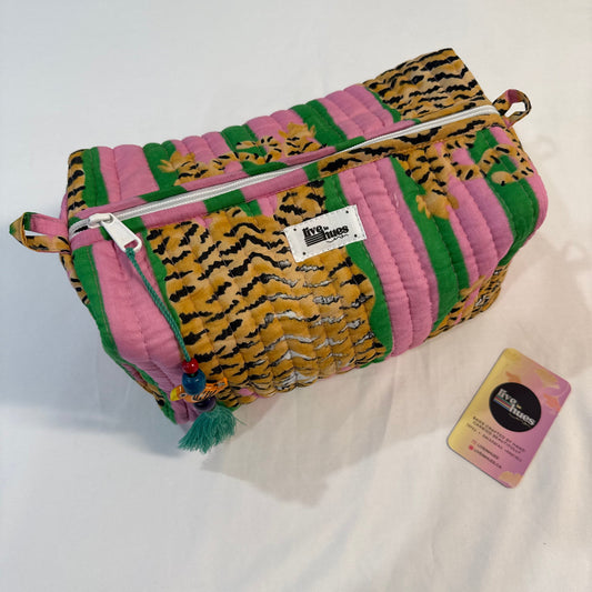 A quilted cosmetic pouch by The Pink Room featuring a colorful patchwork design of pink, green, and tiger-print panels, shown on a white fabric background with its brand card.