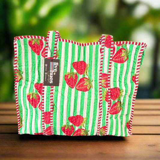 Green and red striped bag with strawberry pattern on a black stand against a white background
