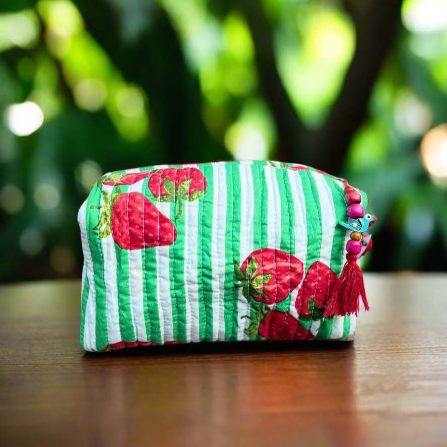 Green and white striped pouch with red strawberry designs on a wooden surface outdoors.