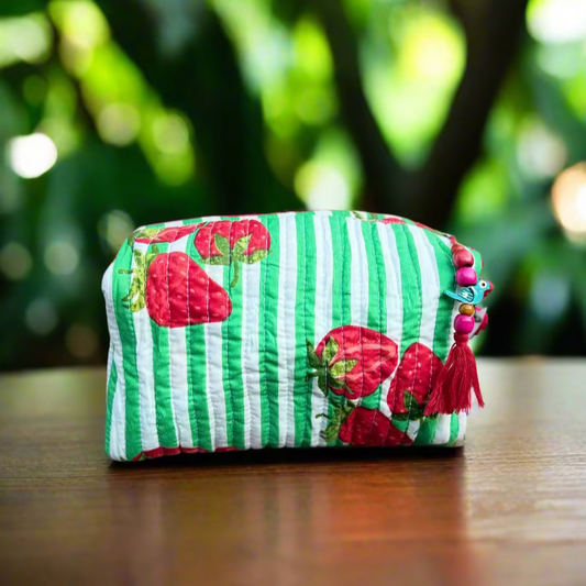 Green and white striped pouch with red strawberry designs on a wooden surface outdoors.